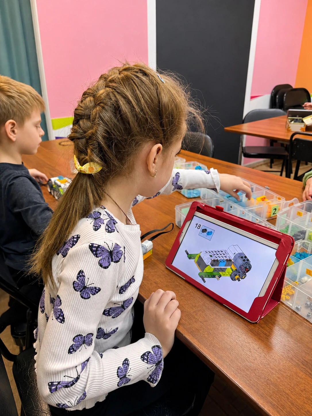 Девочка собирает робота LEGO по инструкции на планшете